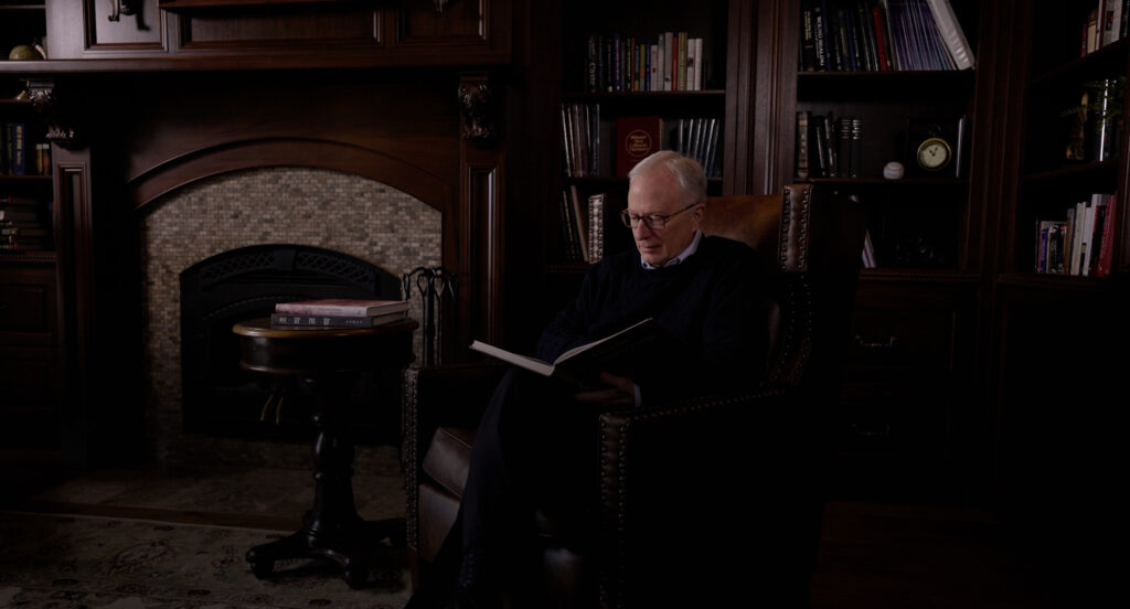 Dr. Lynch in a home library, sitting in a chair reading a book