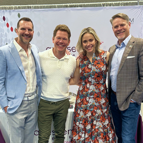 Four people standing and smiling in front of an ariessence pure PDGF+ conference booth display